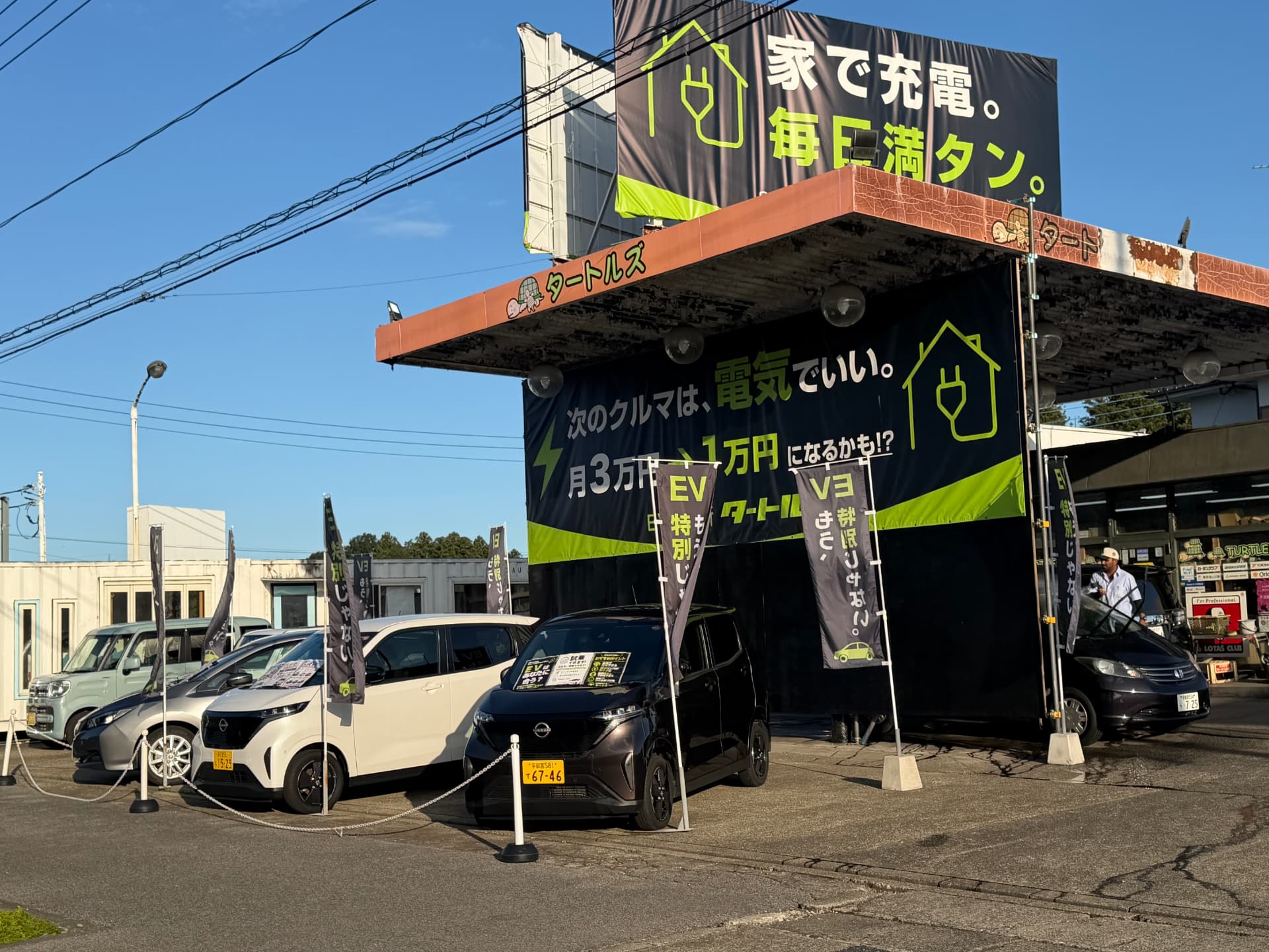 「家で充電。毎日満タン。」の看板とEVが並ぶ店舗の様子